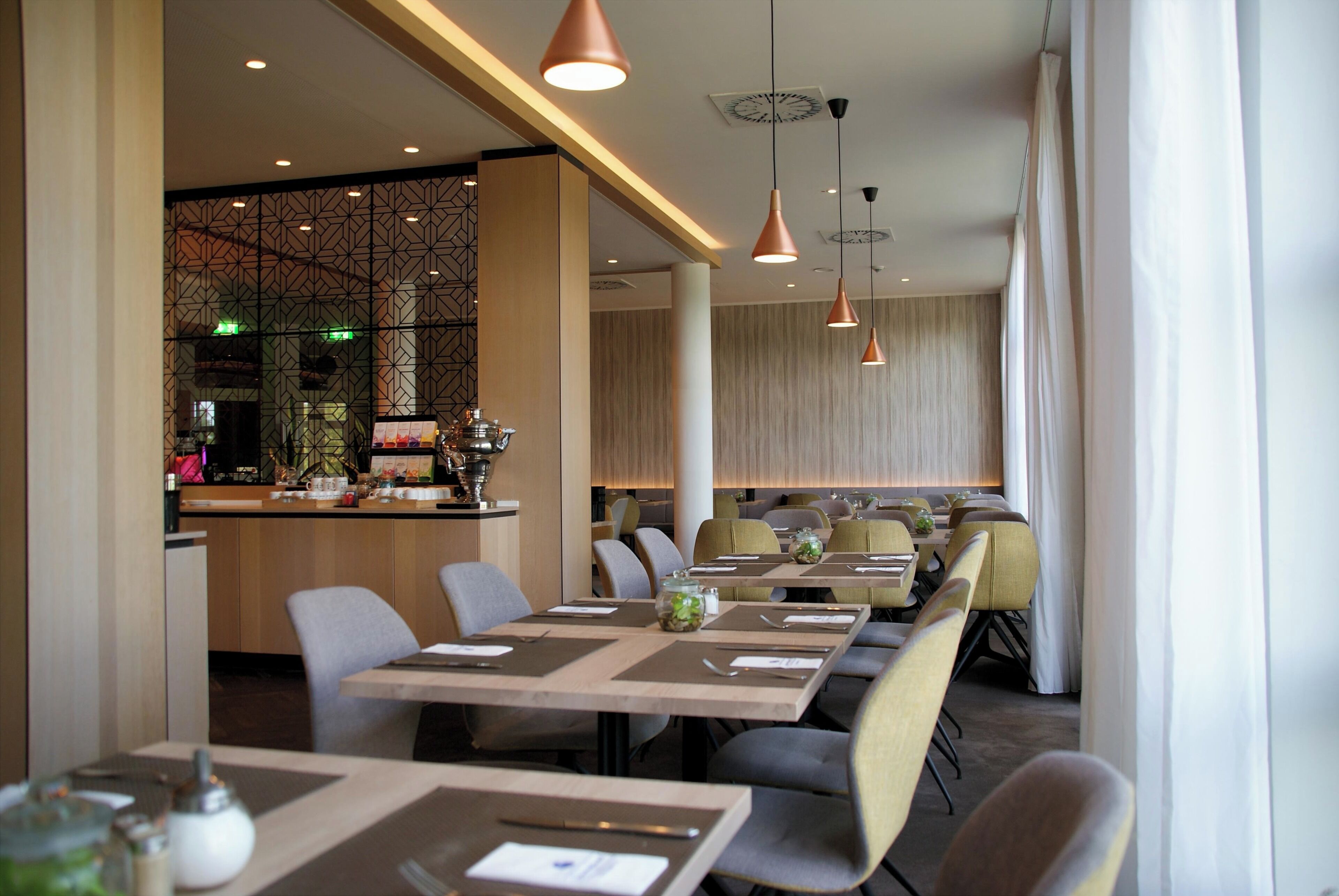 A restaurant interior with multiple dining tables, chairs, pendant lighting, and a bar area.