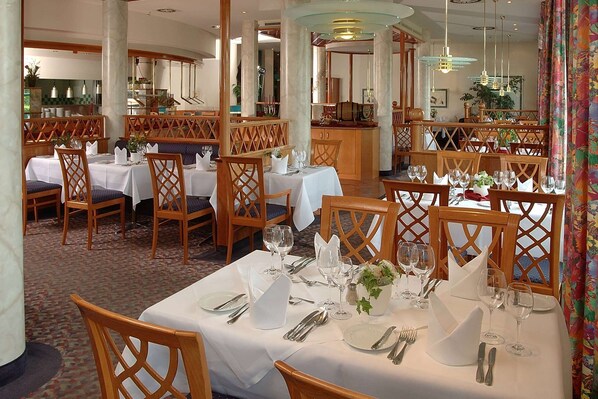 A restaurant with multiple tables set for dining, featuring white tablecloths, wooden chairs, and neatly arranged cutlery.