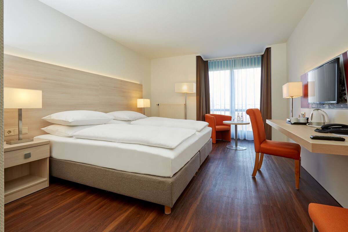 Een hotelkamer met een groot bed, een bureau met stoel, een televisie en een raam met gordijnen.