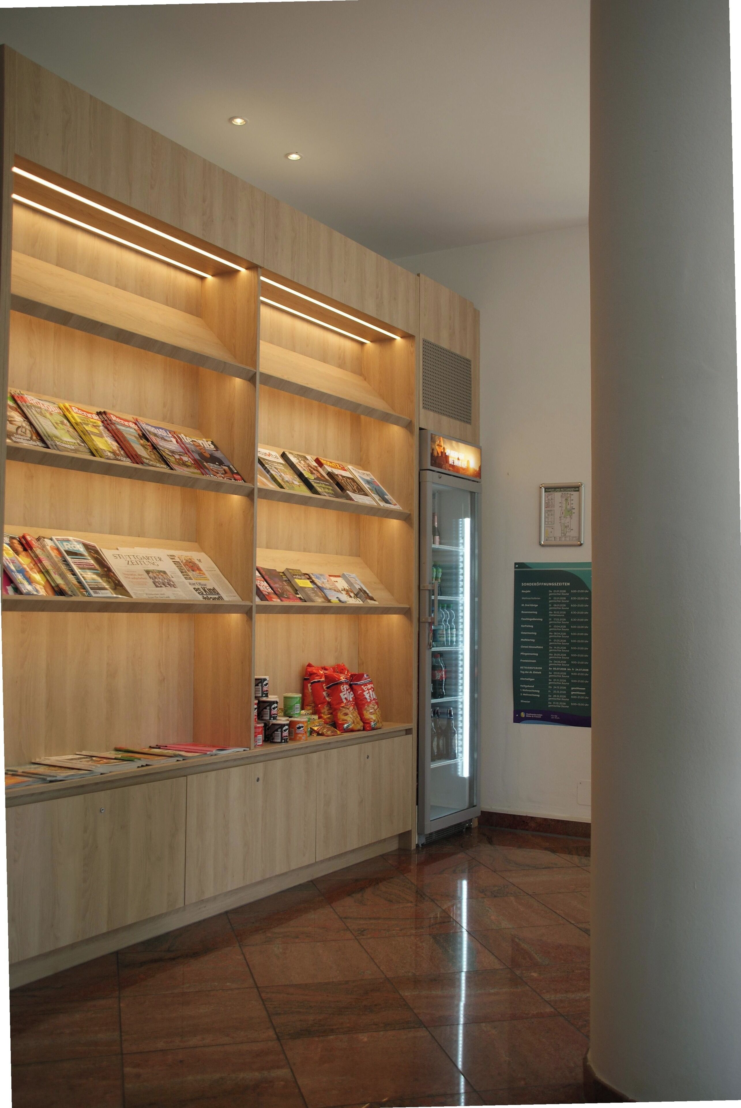 Un espace d’accueil d’hôtel comprenant un comptoir de réception en bois, une vitrine en verre contenant des magazines et un panneau d’affichage fixé au mur.