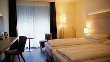 Una camera d'albergo con un letto, una scrivania, una sedia, una lampada e una finestra con tende.