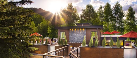 A modern outdoor seating area with a stone wall, red umbrellas, and a staircase leading to an upper level.