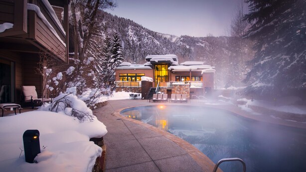Un área de spa con un jacuzzi, paisajes nevados y un edificio con grandes ventanales.