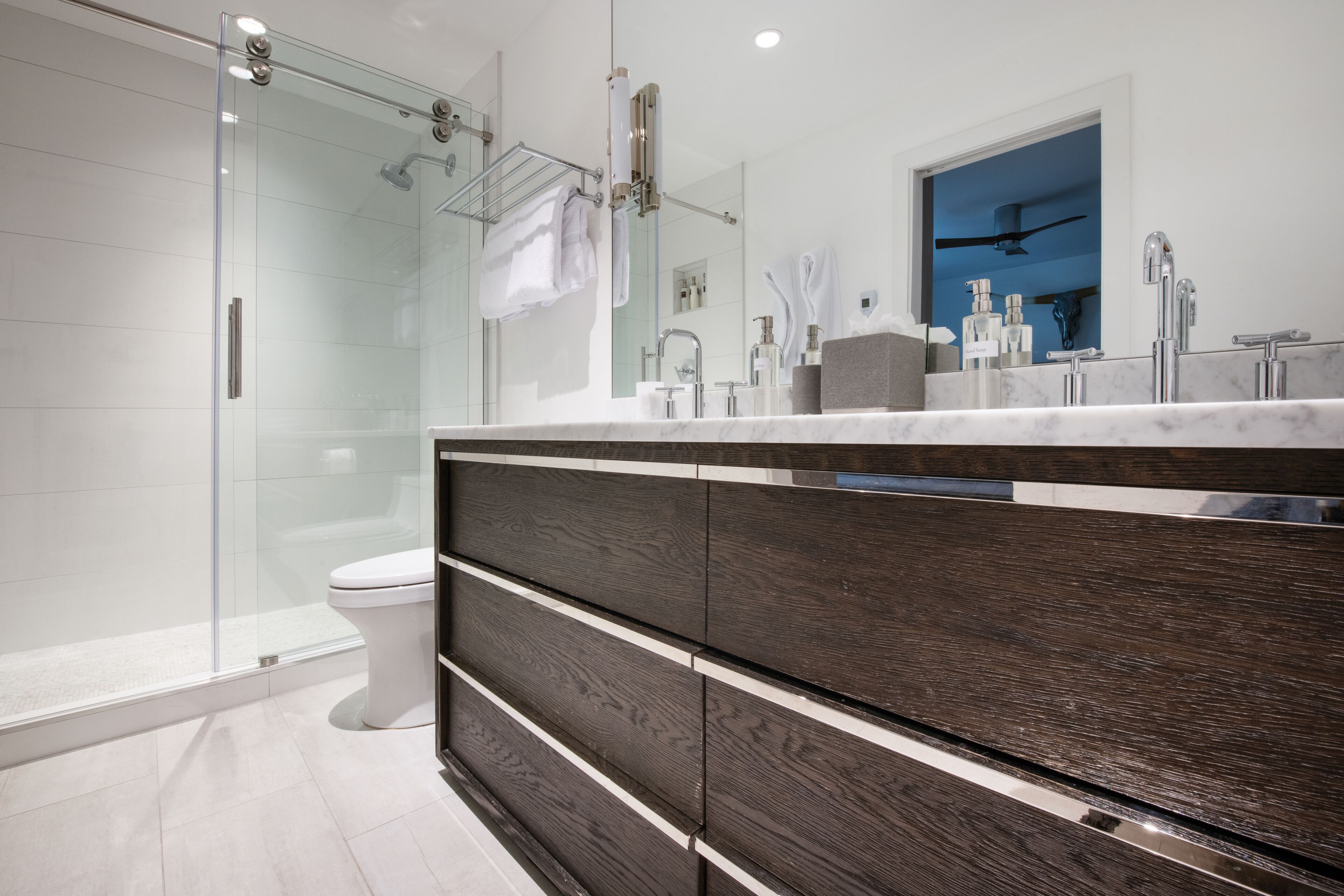 Un bagno moderno con cabina doccia in vetro, un ampio lavabo con finitura in legno scuro e uno specchio che riflette l'ambiente.