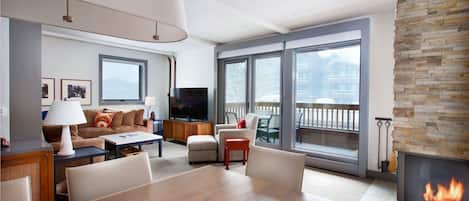 A modern living room with a fireplace, large windows, and a flat-screen TV.
