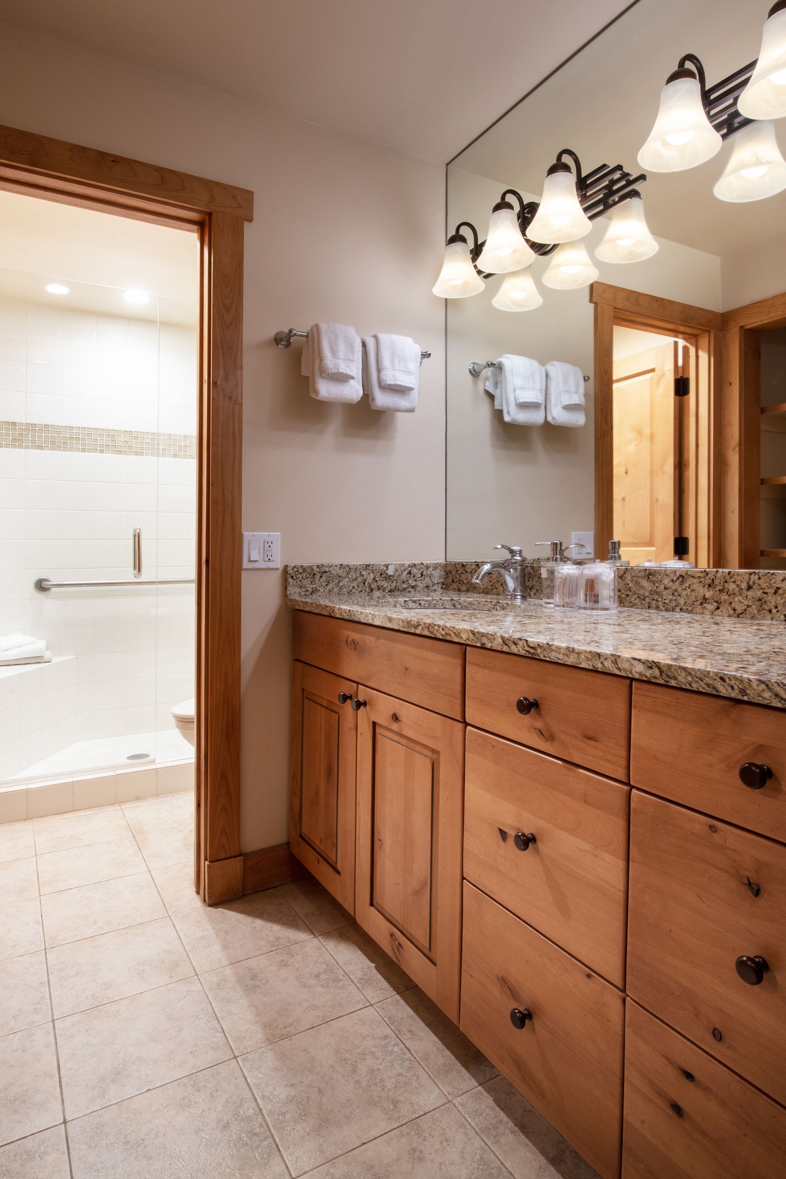 A bathroom with a granite countertop, wooden cabinets, a large mirror, and a shower area.