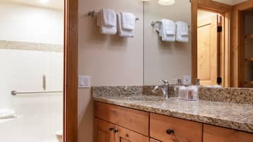 A bathroom with a granite countertop, wooden cabinets, a large mirror, and a shower area.