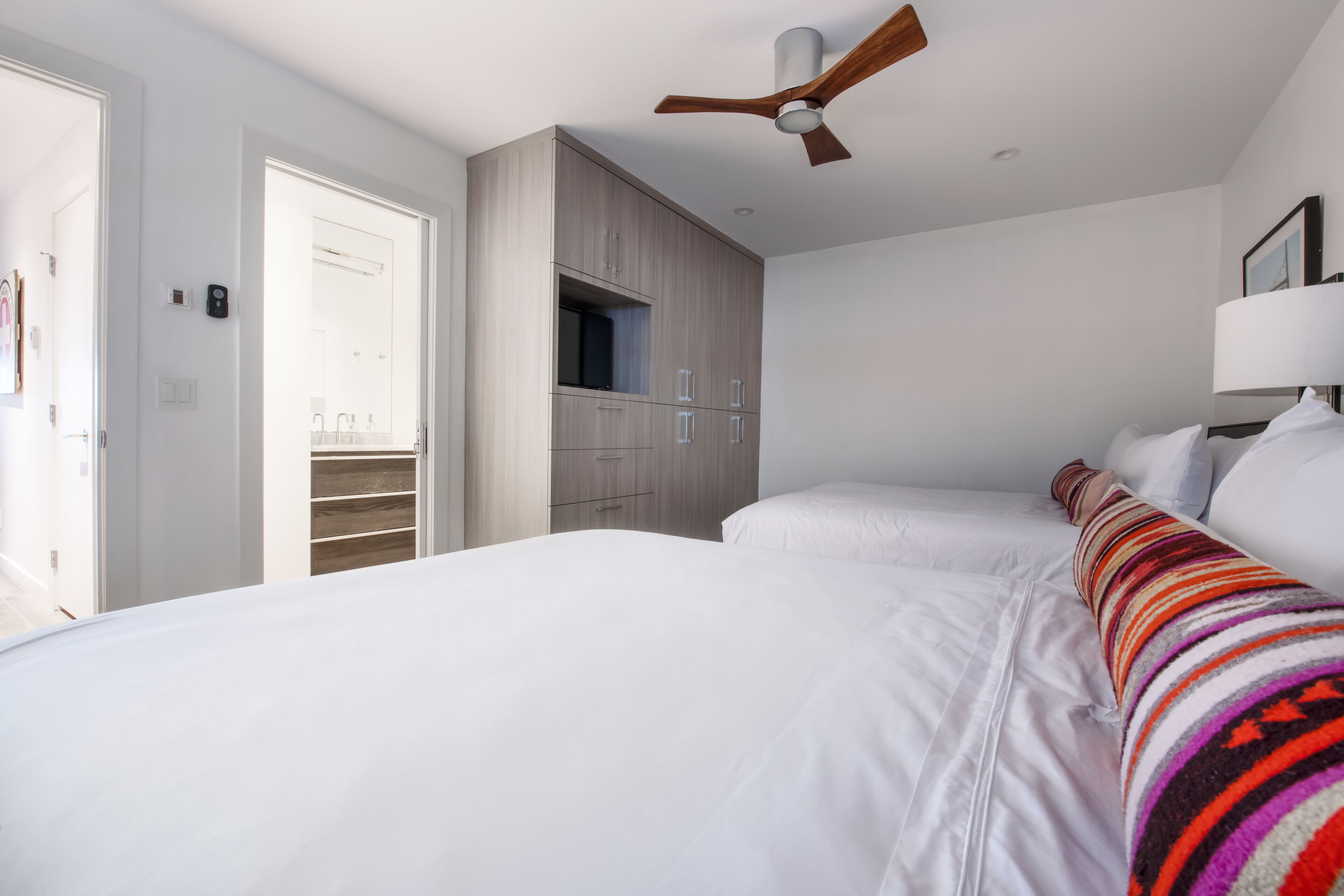 A modern hotel room with two beds, a ceiling fan, and a walk-in closet.