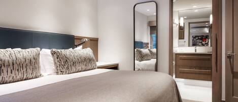 A modern hotel room with a large bed, a bedside table, a mirror, and a view of the bathroom.