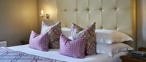 A neatly made bed with patterned pillows and a headboard, a bedside table with a lamp, and a wall-mounted light fixture.