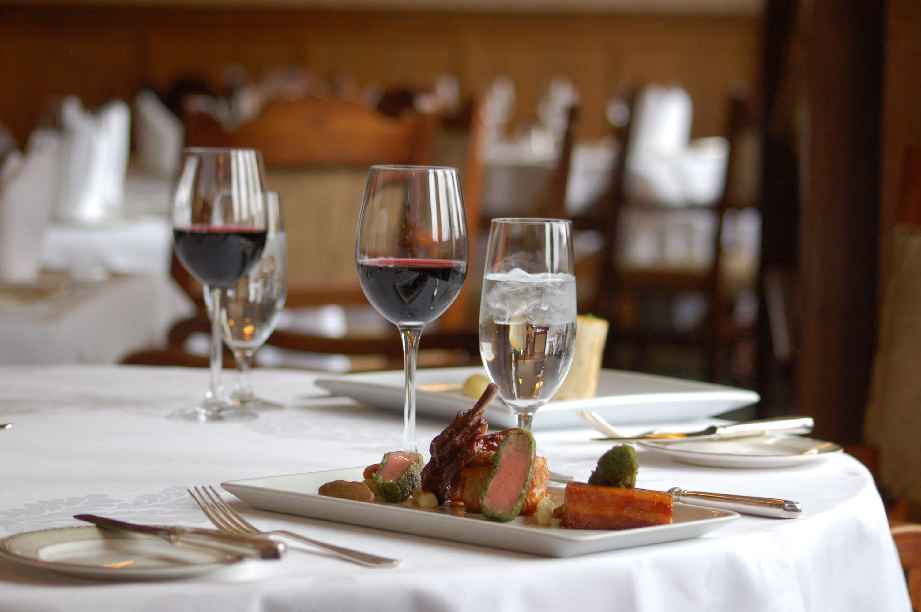 A dining table set with plates, cutlery, and glasses of wine.