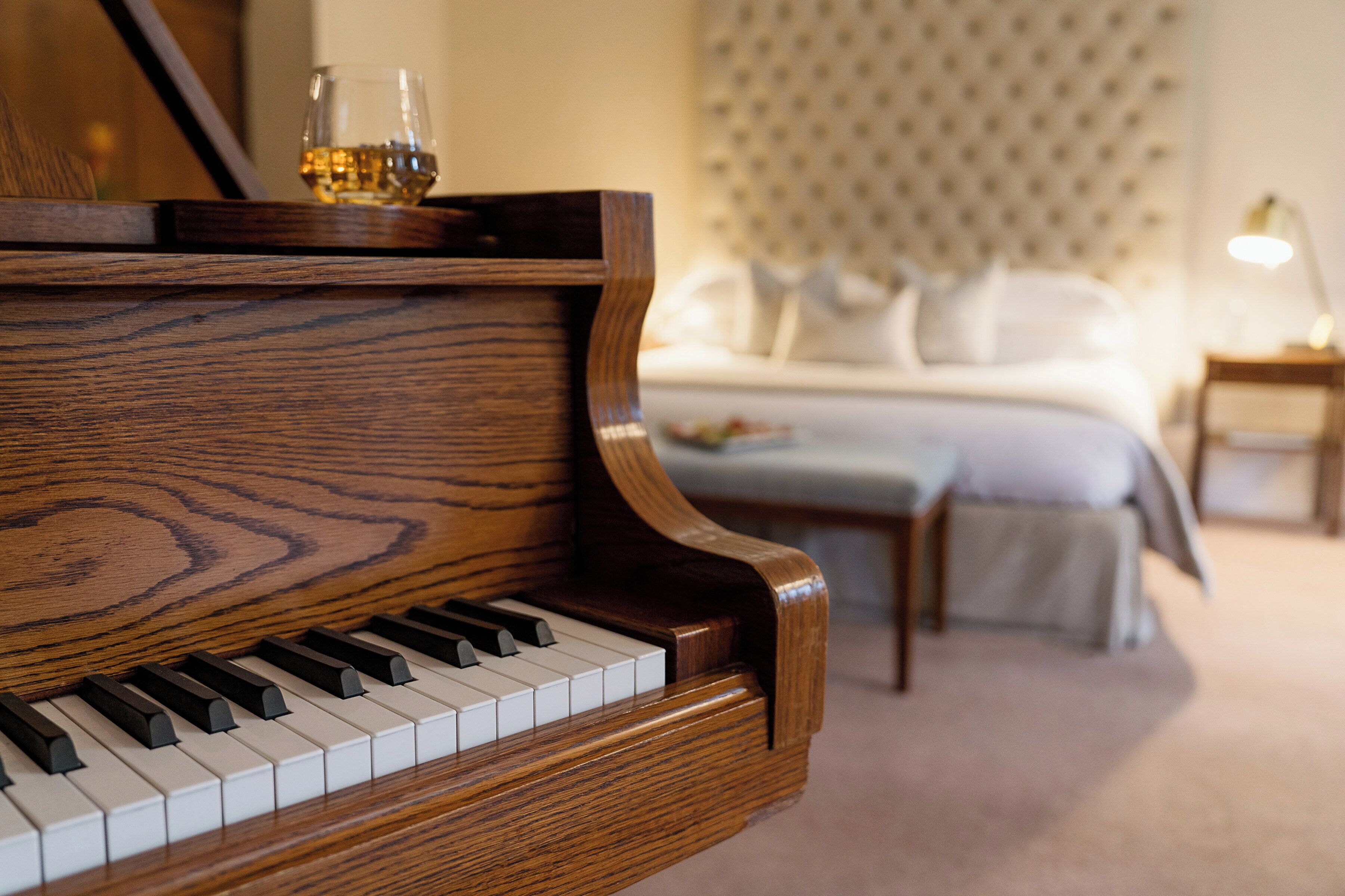 A grand piano in a hotel room with a bed and a nightstand.