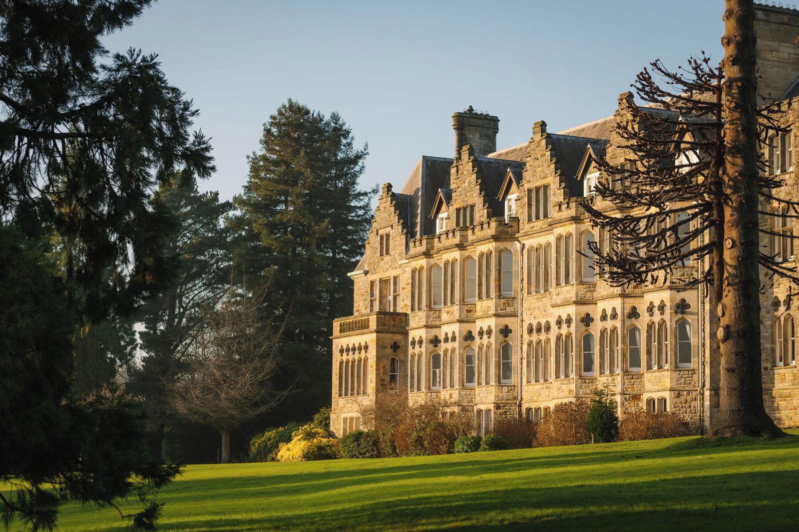 A large stone building with multiple windows and a symmetrical facade, surrounded by a well-maintained lawn and trees.