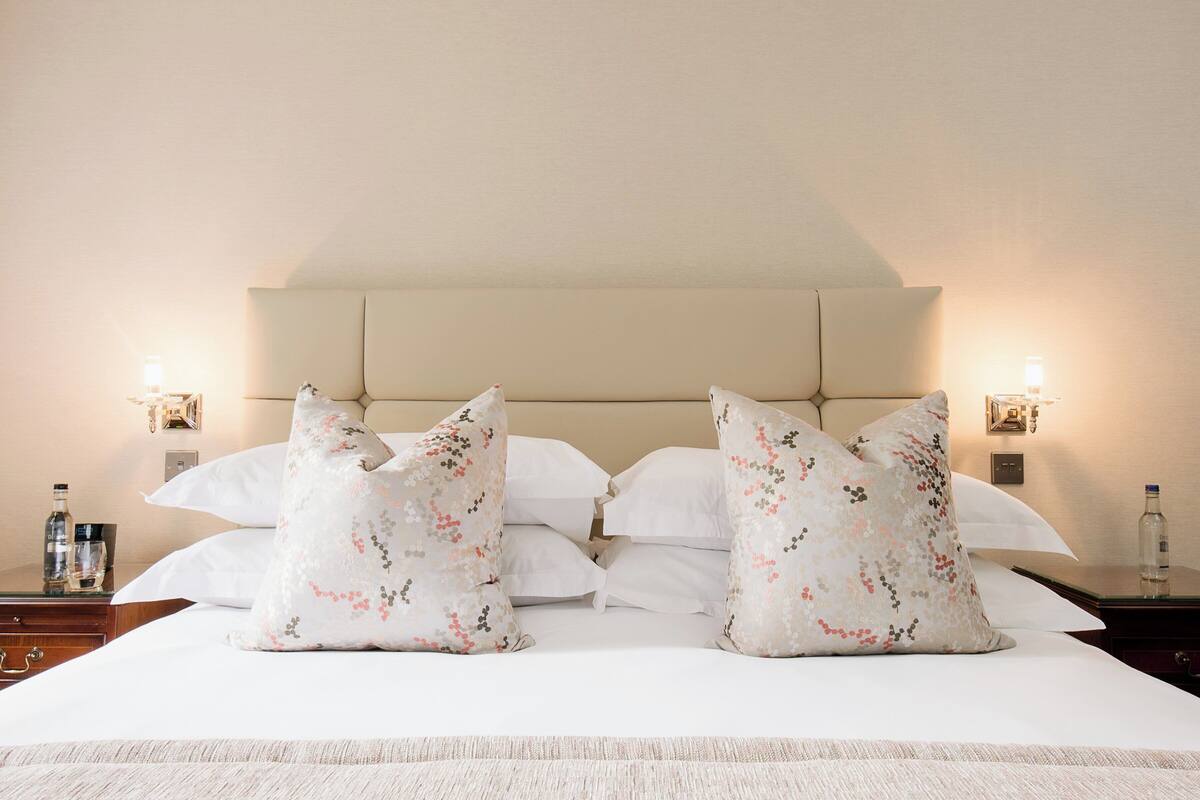 A neatly made bed with floral-patterned pillows, a headboard, and two bedside lamps.