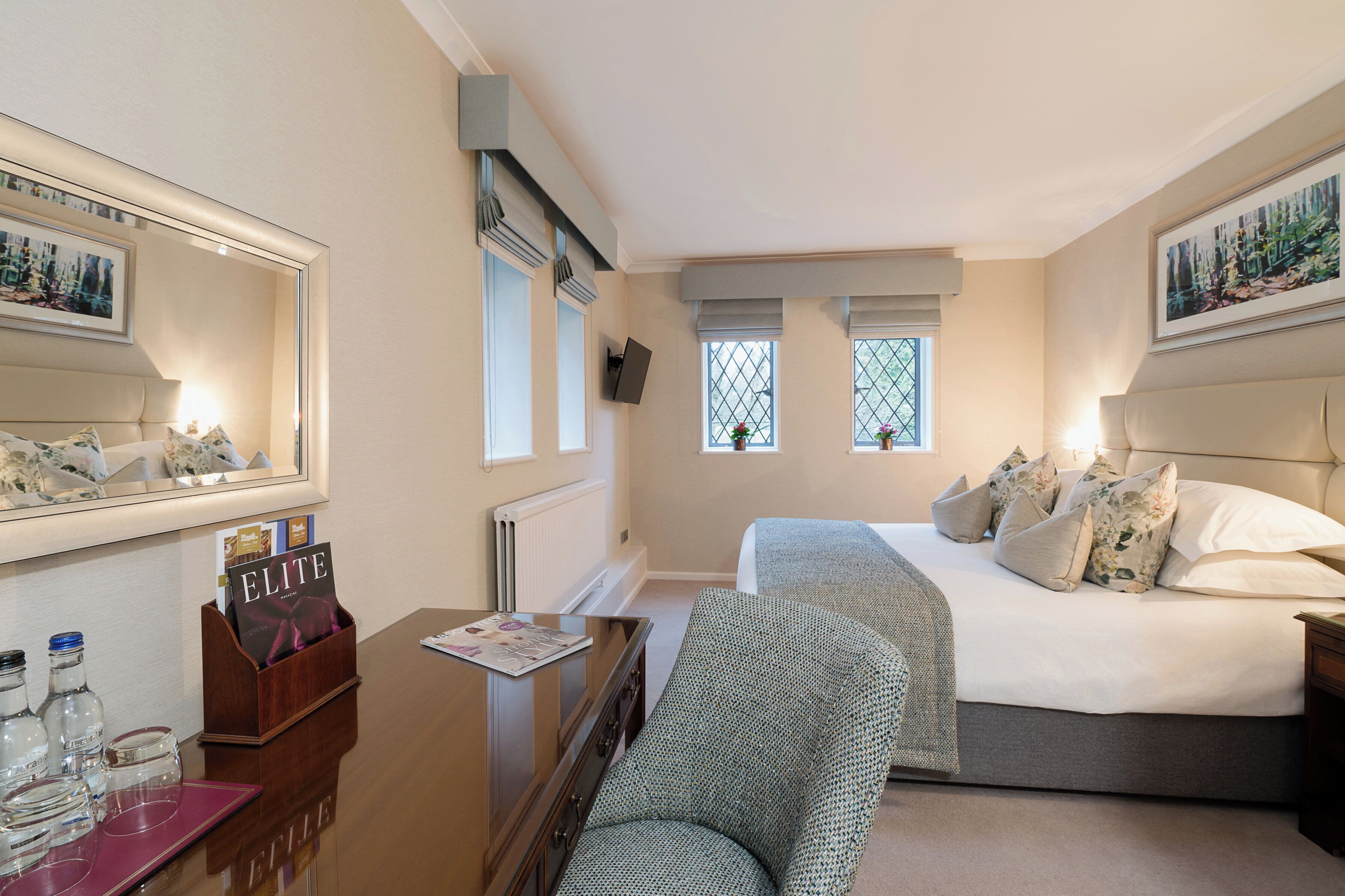 Una habitación de hotel con cama, una silla, un escritorio con espejo y una ventana.