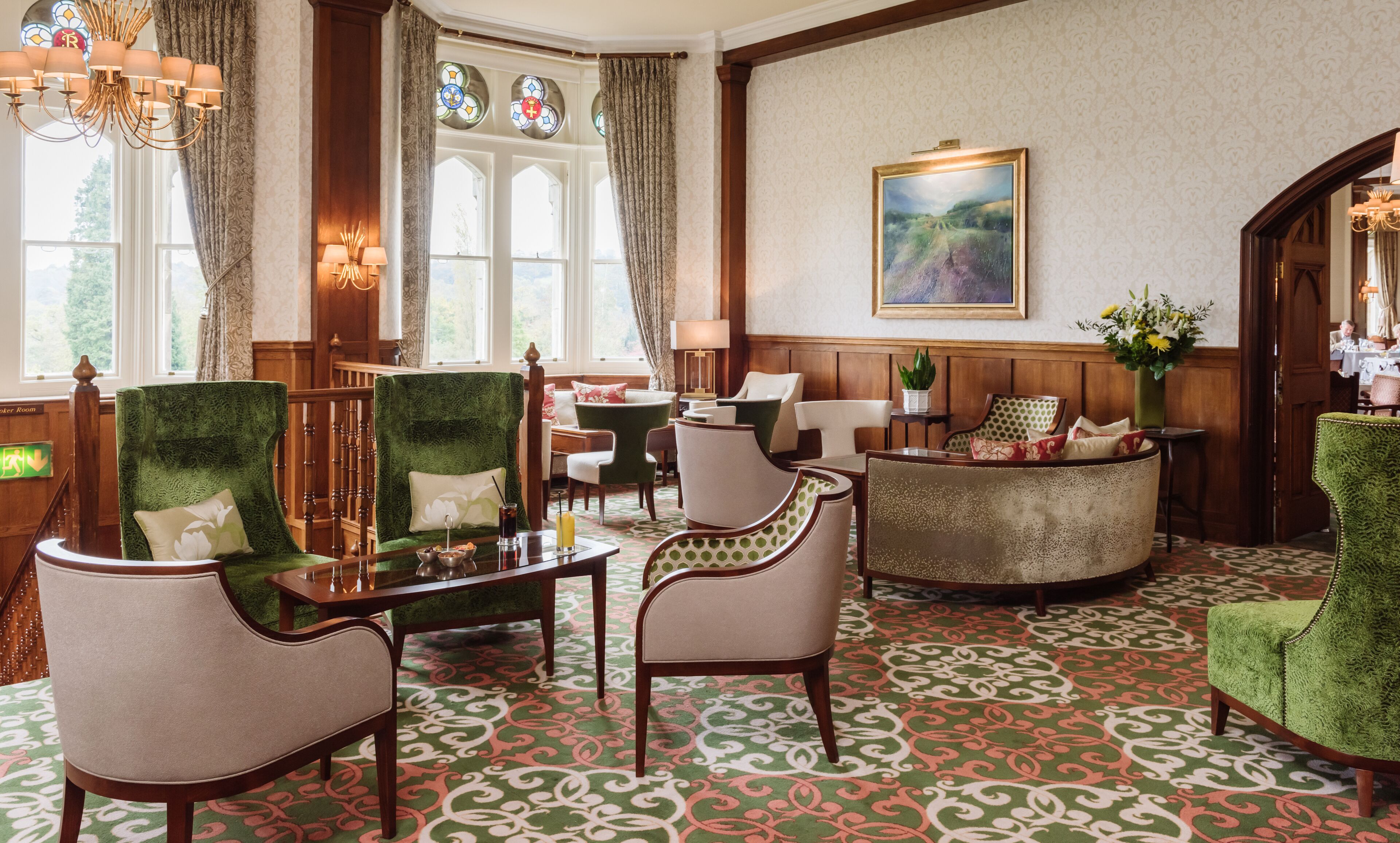 A hotel lobby with green upholstered chairs, a wooden reception desk, and a patterned carpet.