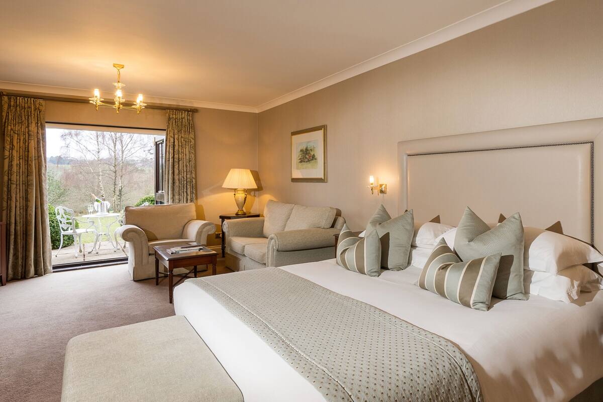 A hotel room with a large bed, two armchairs, a small table, and a window with curtains.