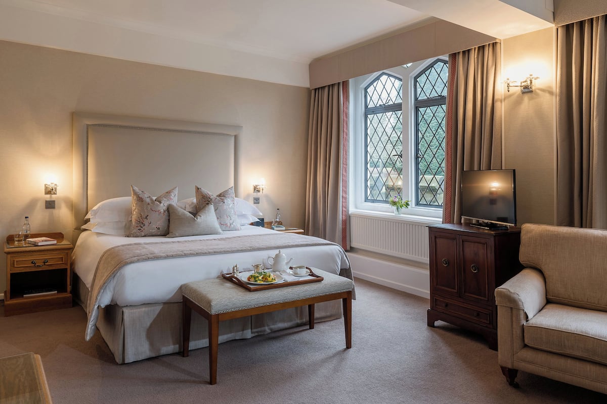 A neatly arranged bedroom with a large bed, bedside tables, a television, and a window with curtains.