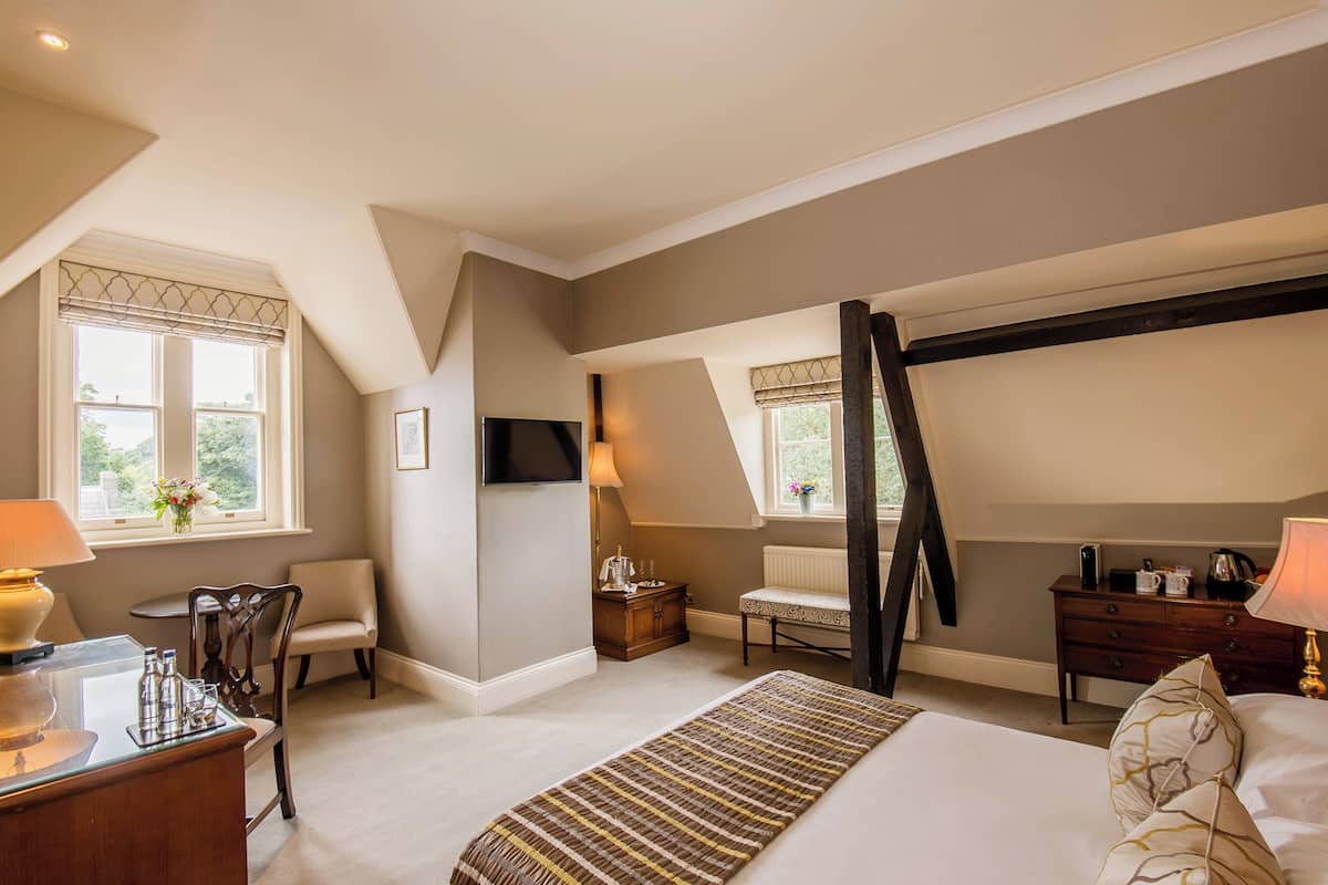 A bedroom with a bed, a desk, a chair, a lamp, a TV, and a window.
