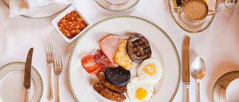 Un desayuno con huevos, salchichas, tomates y morcilla, acompañado de salsas y utensilios.