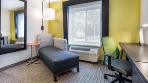 Une chambre d’hôtel avec un canapé, une petite table, une chaise, une grande fenêtre donnant sur des arbres et un miroir au mur.