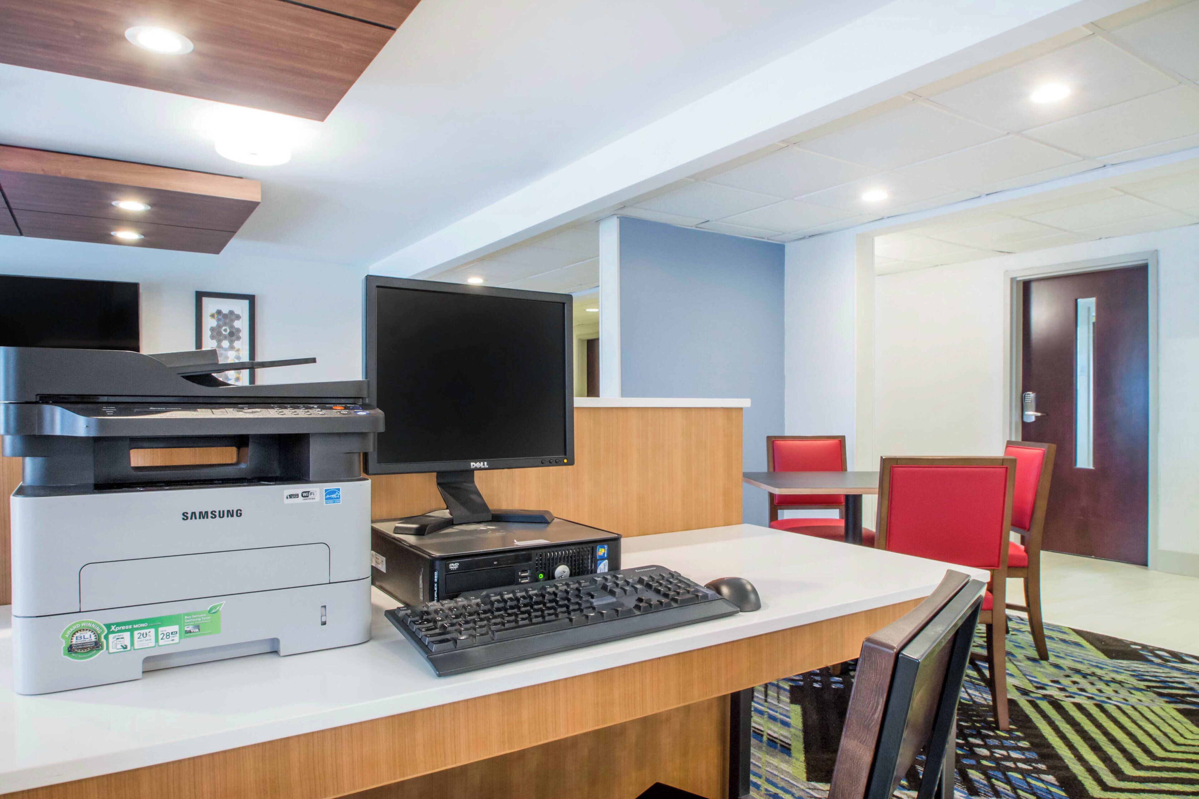A hotel reception desk with a printer, monitor, keyboard, and a red chair.