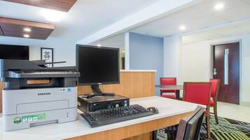 A hotel reception desk with a printer, monitor, keyboard, and a red chair.