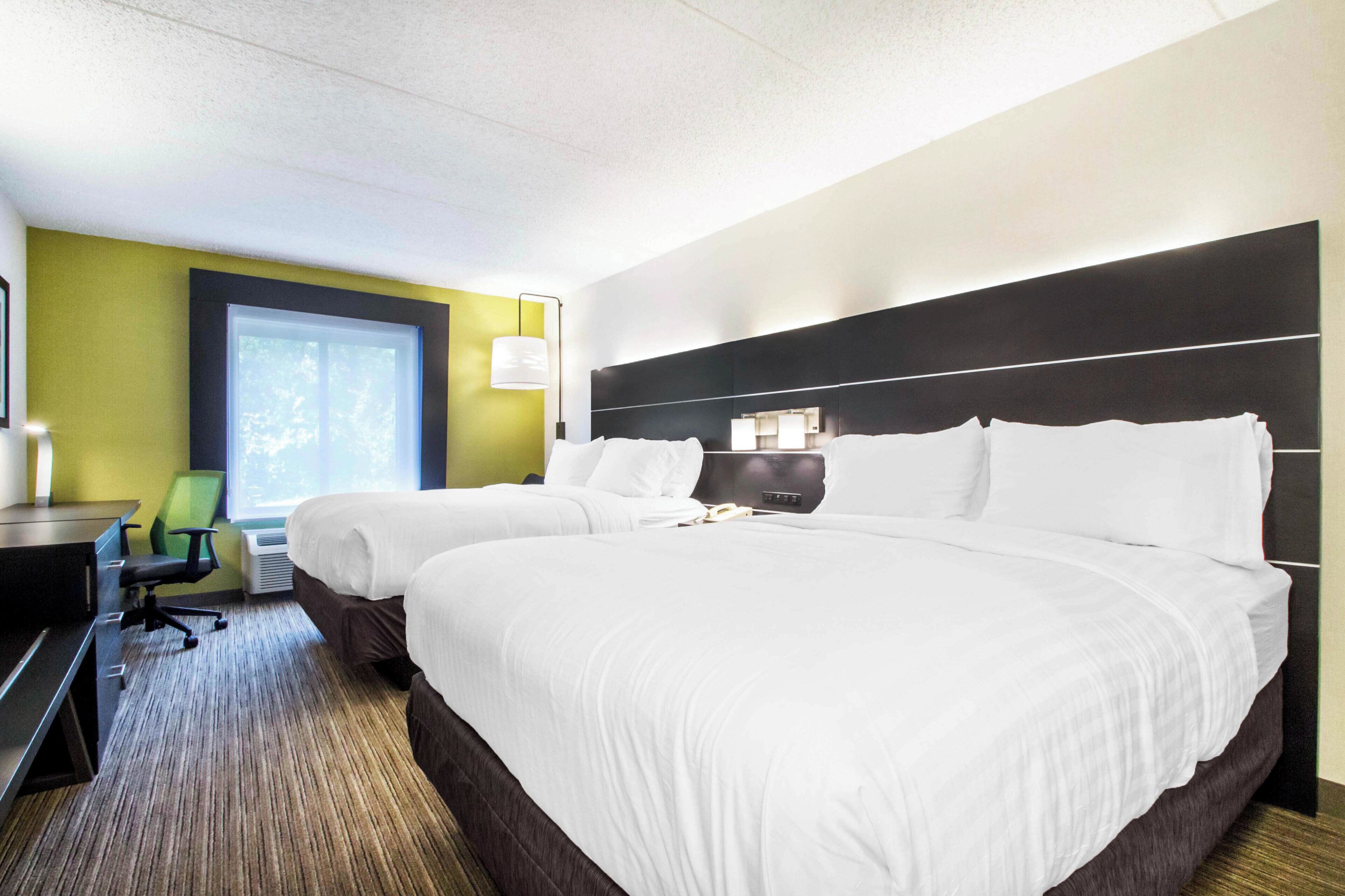 A hotel room with two beds, a desk, a chair, and a window.