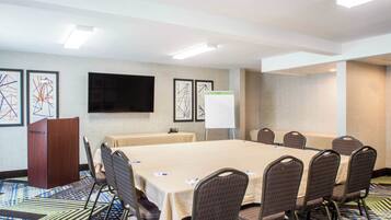 A conference room with a long table, chairs, a podium, a whiteboard, and framed abstract art on the walls.