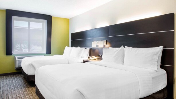 Une chambre d’hôtel avec deux lits, une grande fenêtre, un climatiseur fixé au mur et une table de chevet avec une lampe.