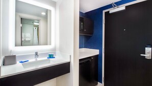 Une salle de bain moderne avec un lavabo blanc, un miroir, un meuble noir, un four à micro-ondes et une porte sombre.