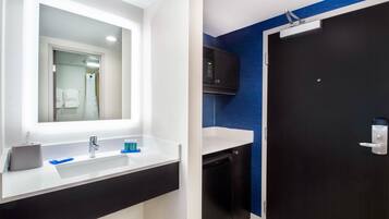 Un baño moderno con un lavabo blanco, un espejo, un mueble negro, un microondas y una puerta oscura.