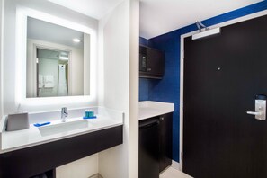 Un baño moderno con un lavabo blanco, un espejo, un mueble negro, un microondas y una puerta oscura.
