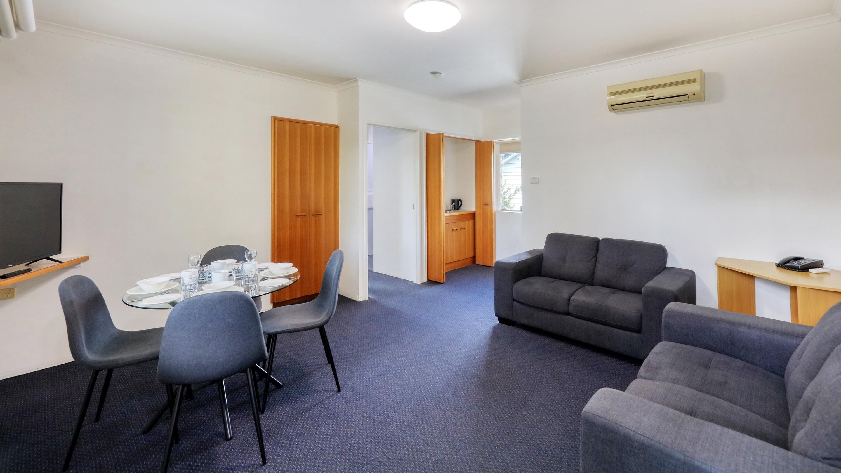Una habitación de hotel moderna con zona de comedor, sofá, televisión y aire acondicionado.