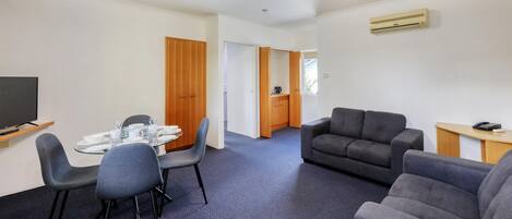 Una habitación de hotel moderna con zona de comedor, sofá, televisión y aire acondicionado.