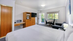 Ein Hotelzimmer mit einem Bett, einem Holztisch mit Fernseher, einem kleinen Tisch mit Stühlen und einem Fenster mit Blick auf Grünflächen.