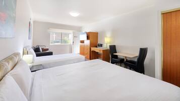 A hotel room with two beds, a desk, a chair, a microwave, and a window with a view of buildings.