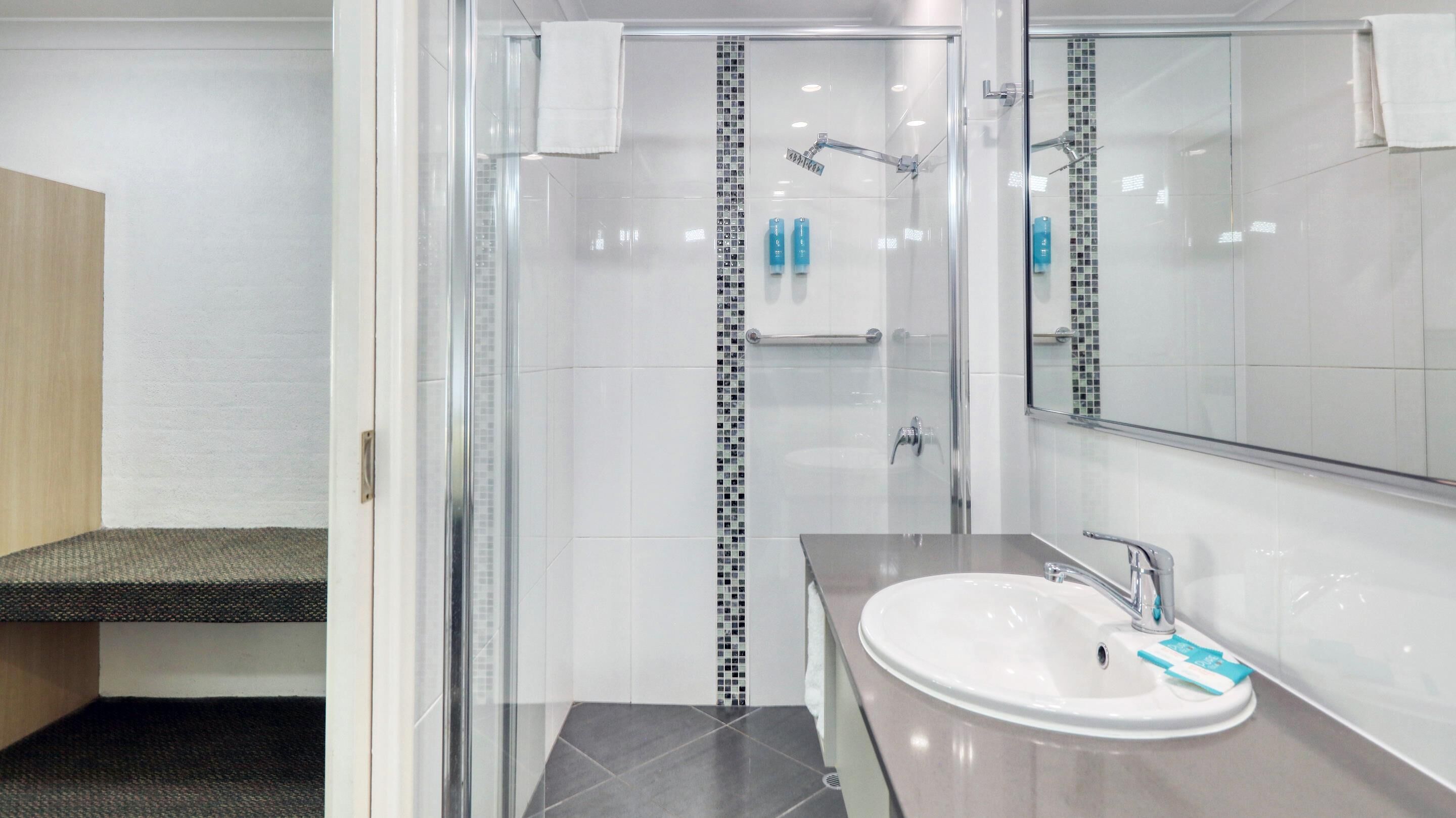A modern bathroom with a glass-enclosed shower, a white sink with a mirror, and a small shelf with toiletries.