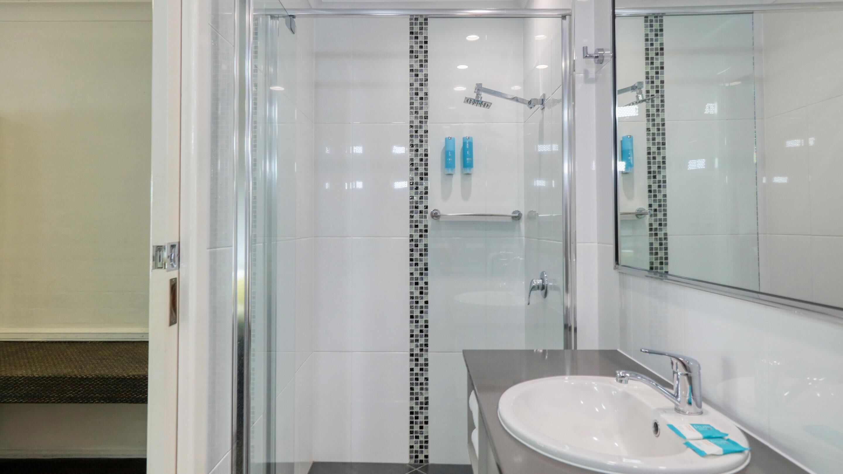 A modern bathroom with a glass-enclosed shower, a white sink with a mirror, and a tiled backsplash.