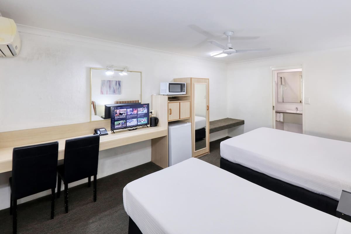 A hotel room with a desk, two beds, a TV, a microwave, and a ceiling fan.