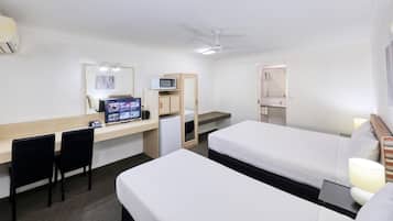 A hotel room with a desk, two beds, a TV, a microwave, and a ceiling fan.