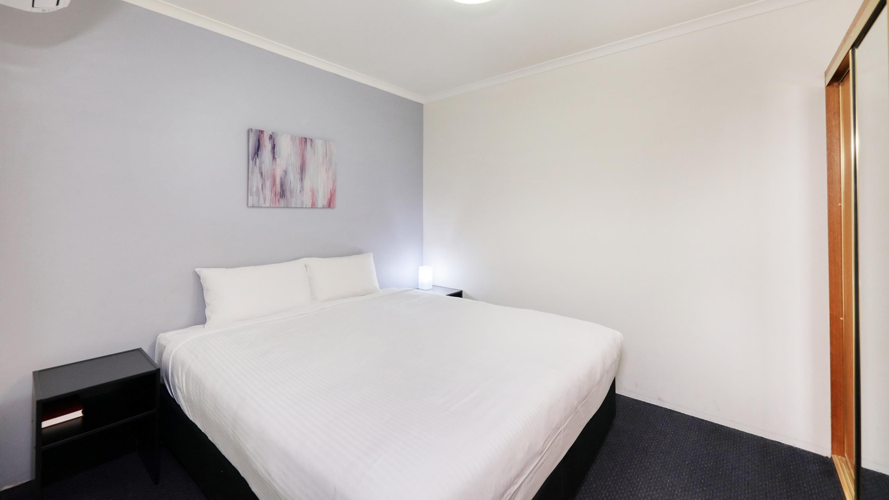 A hotel room with a bed, a nightstand, a wall-mounted light, and a door.