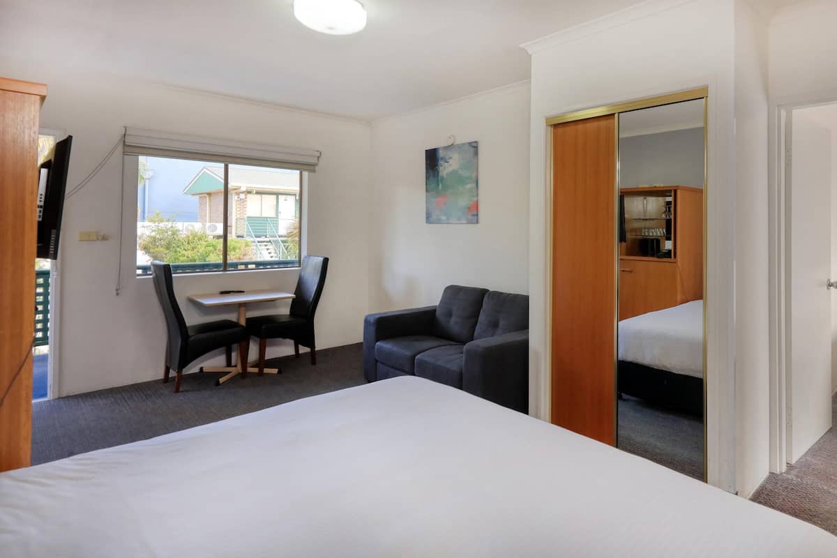 A hotel room with a bed, a desk with a chair, a sofa, and a small table with a lamp.