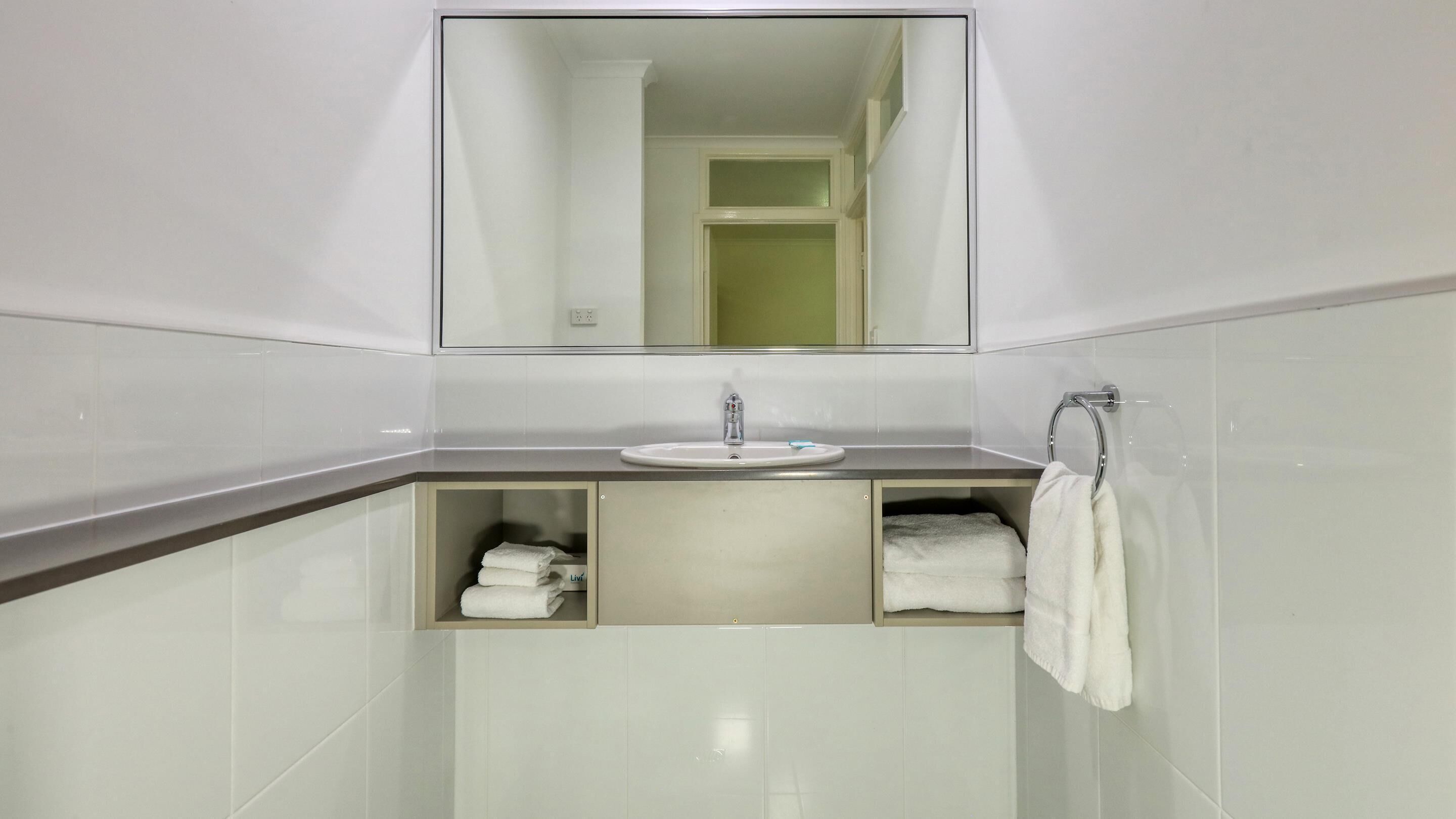 A modern bathroom with a large mirror, a sink, and a towel rack.