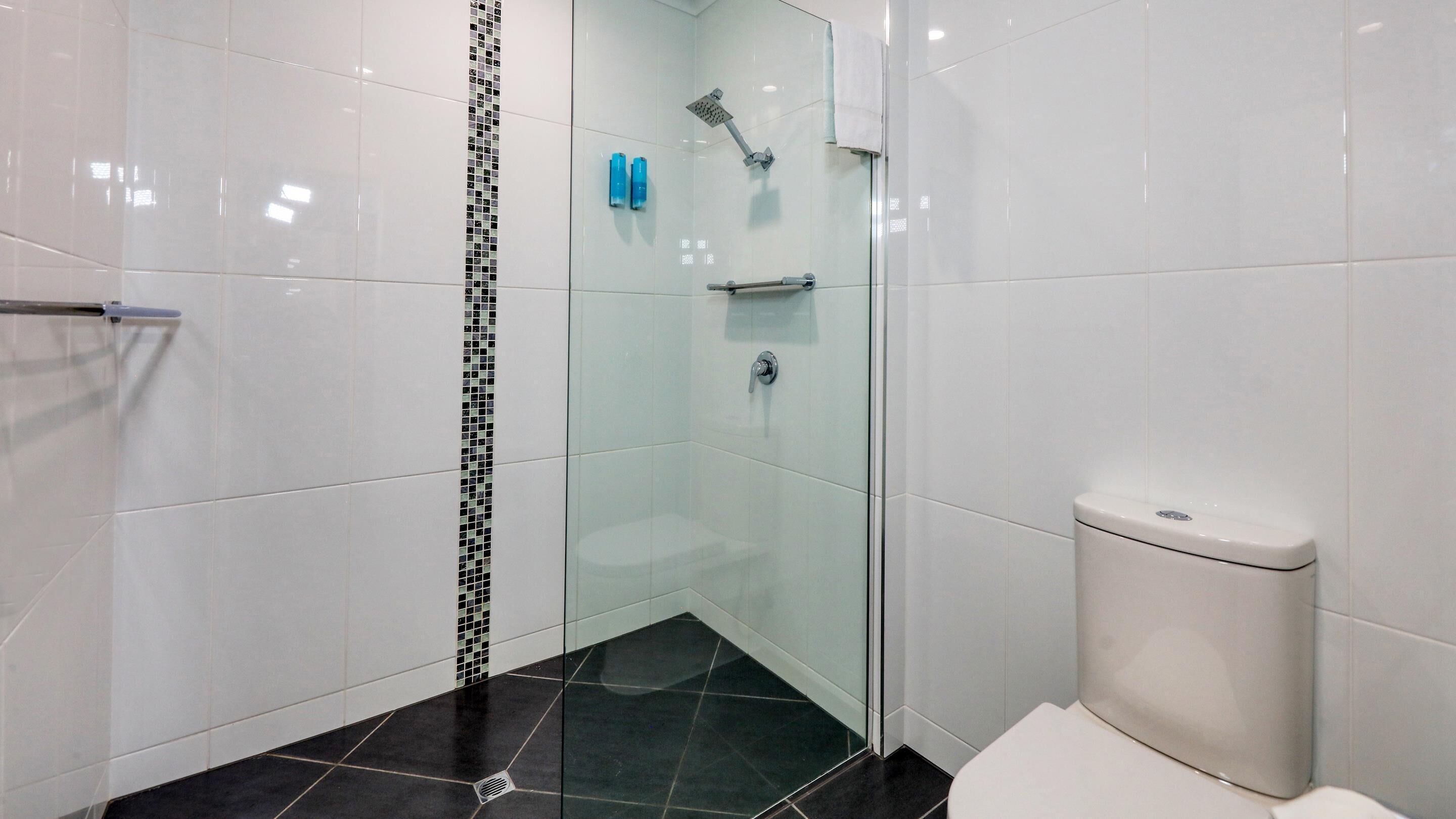 Un baño moderno con cabina de ducha de vidrio, inodoro blanco y suelo de baldosas negras.