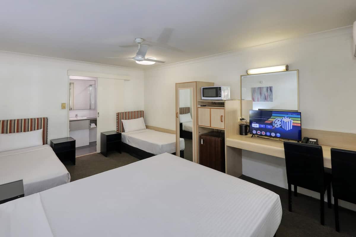 A hotel room with two single beds, a desk with a computer and a flat-screen TV, a microwave, and a small kitchenette.