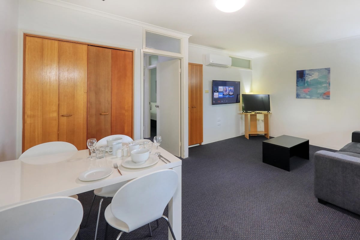 A compact living space with a dining area, a sofa, a TV, and a painting on the wall.