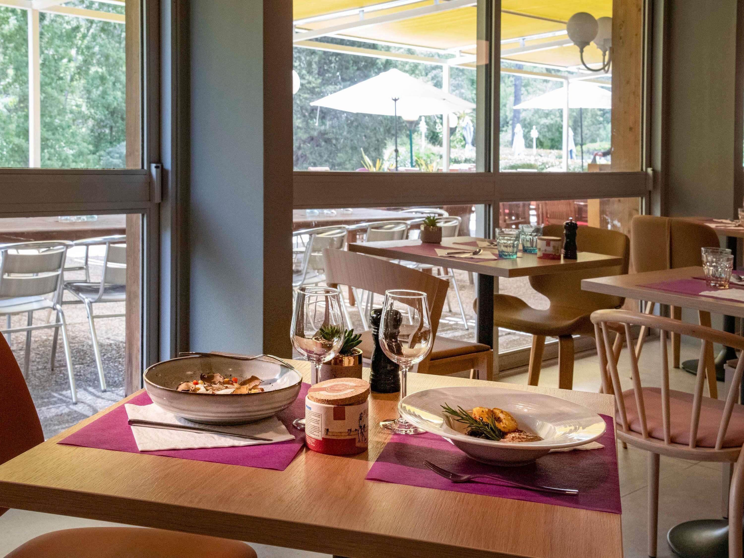 An indoor dining area with tables, chairs, and a view of the outdoors through large windows.