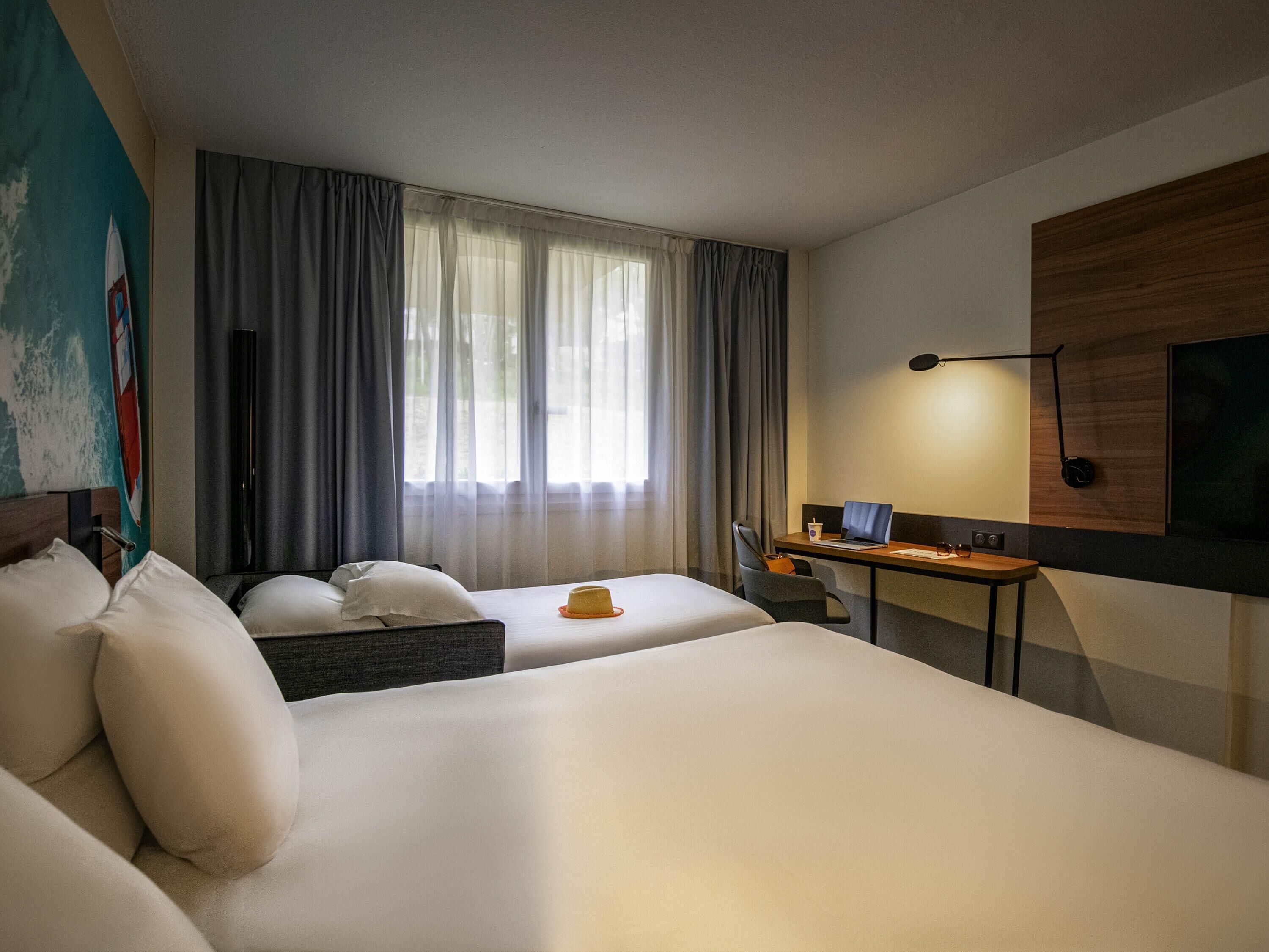 A hotel room with two beds, a desk, a chair, a laptop, and a TV.