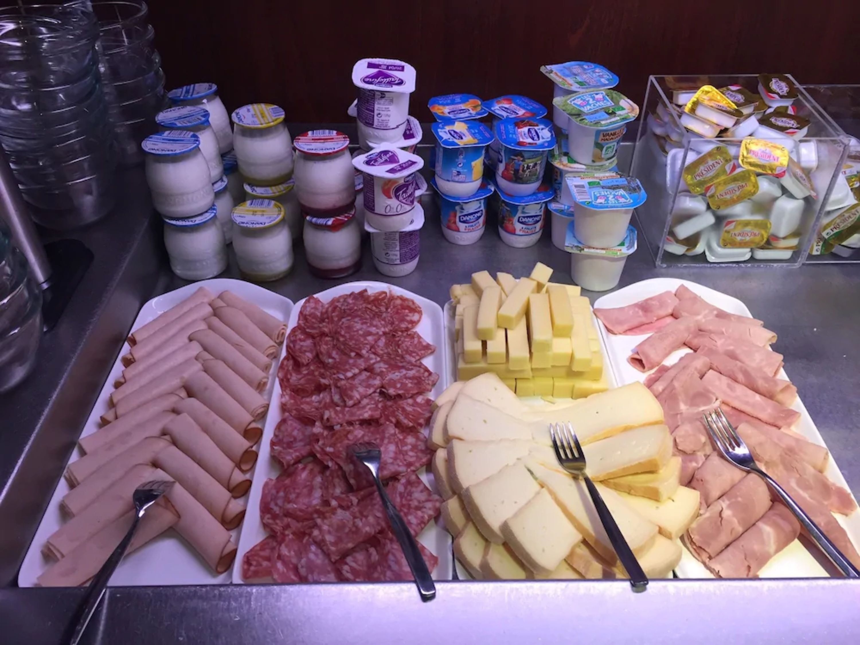 A buffet with various food items including meats, cheeses, and yogurt.